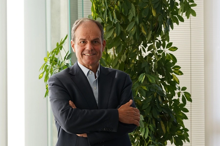 mature man standing in a suit and smiling with tall plant in background inside office